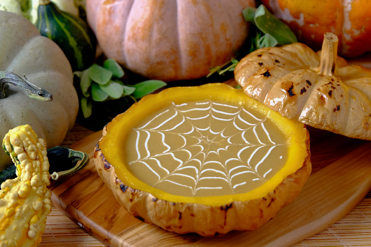 Halloween dip in a pumpkin bowl decorated with a white cobweb, surrounded by autumn pumpkins and gourds.