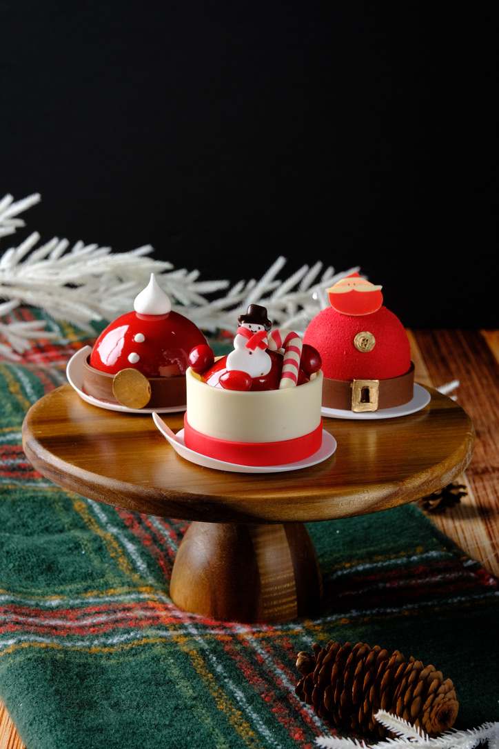 Three festive Daily Garnish mini cakes with Santa and snowman decorations on a wooden cake stand